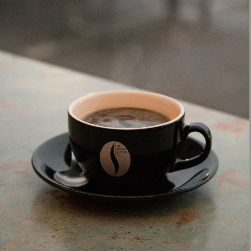 A black Rugga Coffee cup with hot coffee inside
